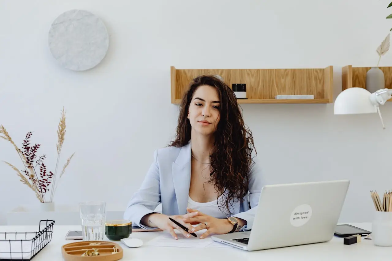 Businesswoman in a light blazer sitting at a desk with a laptop, exuding confidence in a modern office.