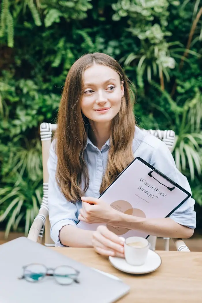 A woman holding a clipboard in a lush, outdoor workspace with greenery.